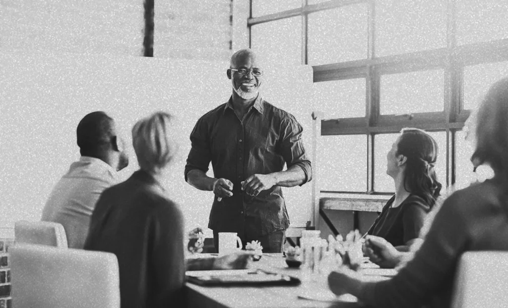man standing in front of a table speaking to a group of people
