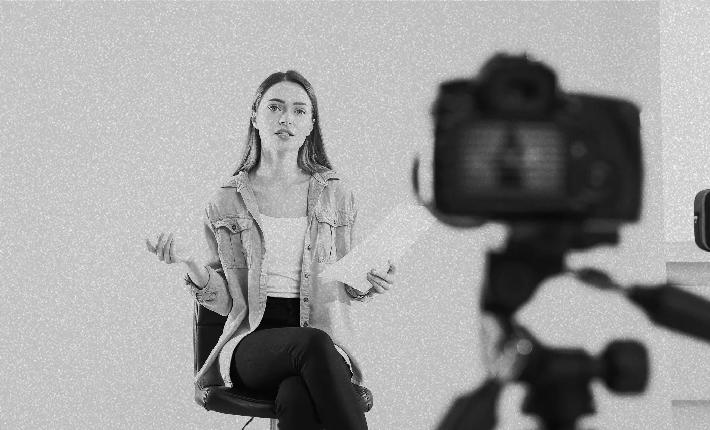 woman sitting in a chair holding a document while being filmed by a camera